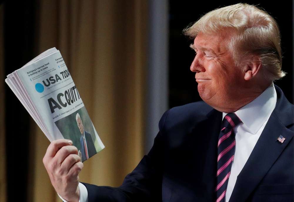 Donald Trump holds up a copy of USA Today front page showing news of his acquittal in his Senate impeachment trial as he arrives to address the National Prayer Breakfast in Washington, February 6, 2020. Reuters/Leah Millis