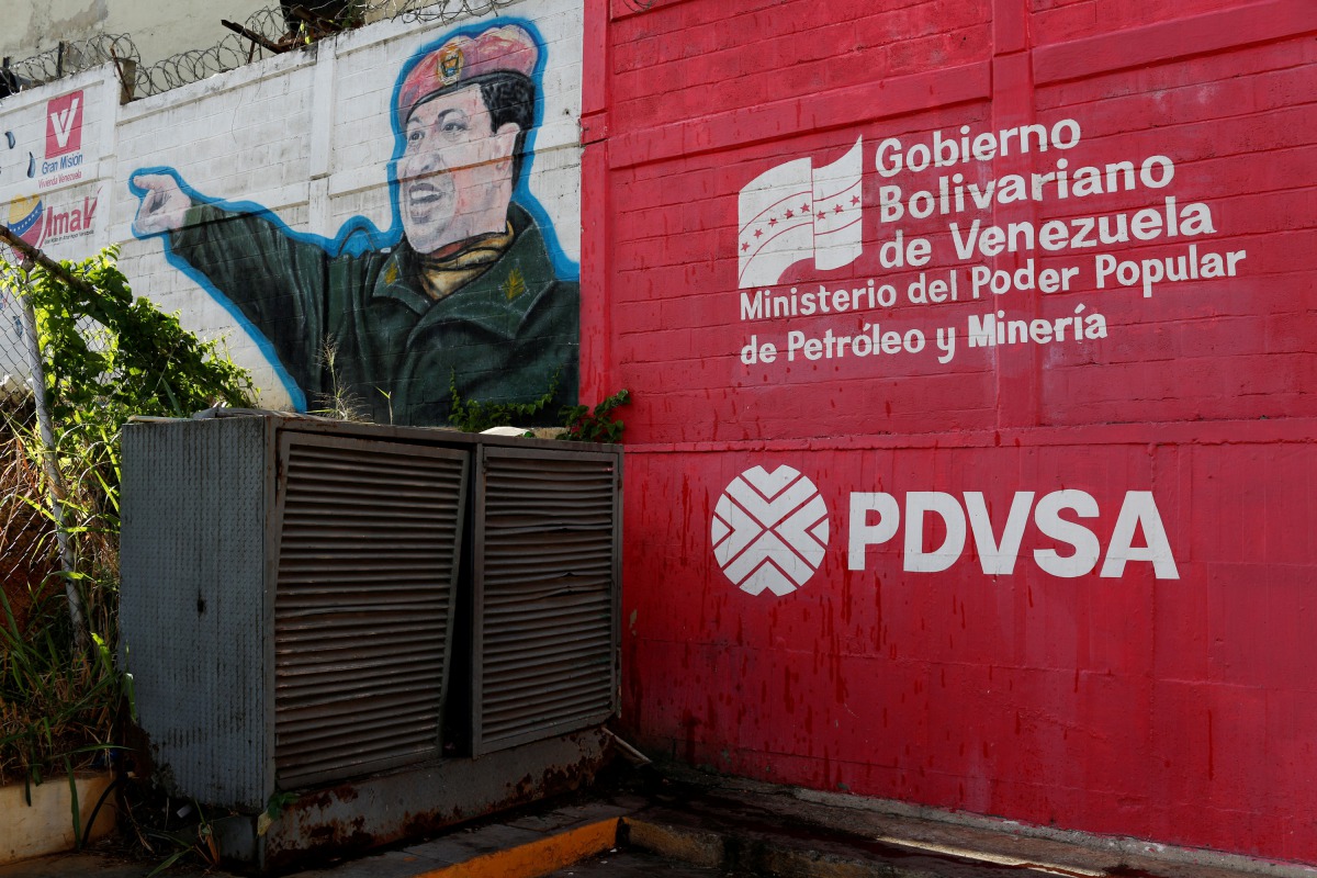 The logo of the Venezuelan state oil company PDVSA is seen next to a mural depicting late President Hugo Chavez at a gas station in Caracas, March 2, 2017. Reuters / Carlos Garcia Rawlins