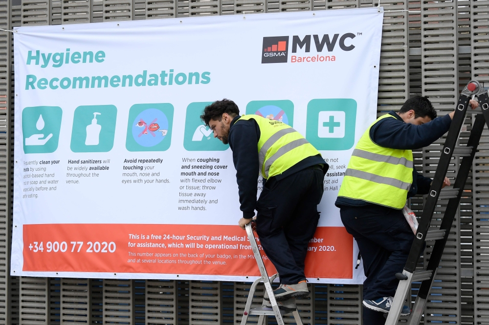 Workers install a banner with hygiene recommendations outside the Mobile World Congress MWC venue on February 12, 2020 at the Fira Barcelona Montjuic centre in Barcelona.  AFP / LLUIS GENE