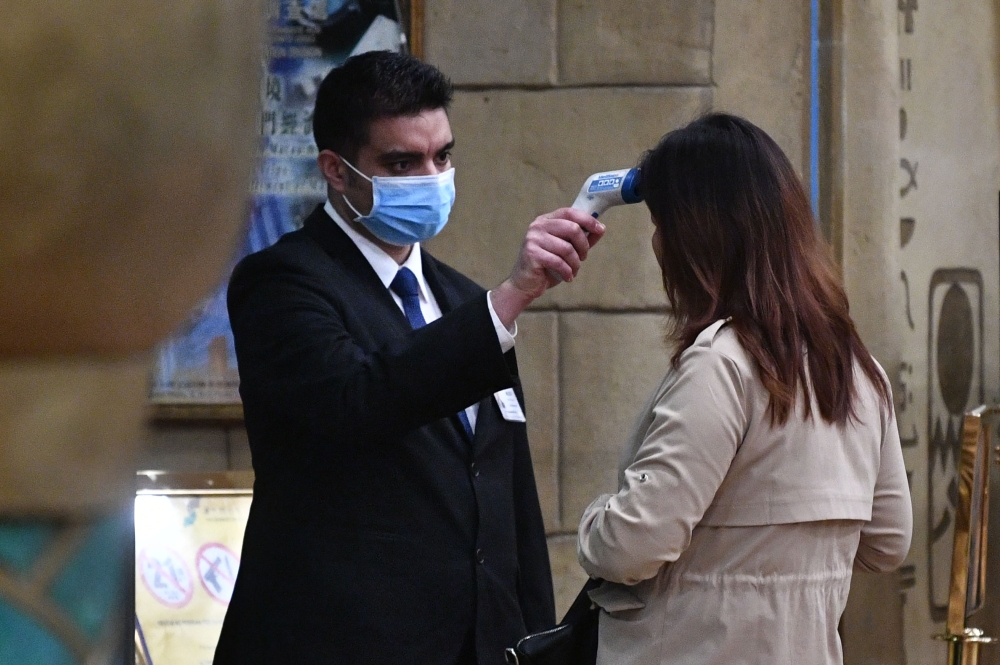 A staff member checks the temperature of a guest entering at a hotel in Macau on January 22, 2020, after the former Portuguese colony reported its case of the virus that originated from Wuhan in China. AFP / Anthony Wallace