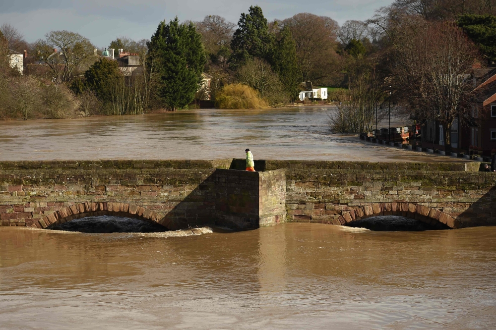 A man walks on the Old Bridge in Hereford, western England, on February 17, 2020, as the waters of the swollen River Wye fill the arches in the aftermath of Storm Dennis.  AFP / Oli Scarff
 