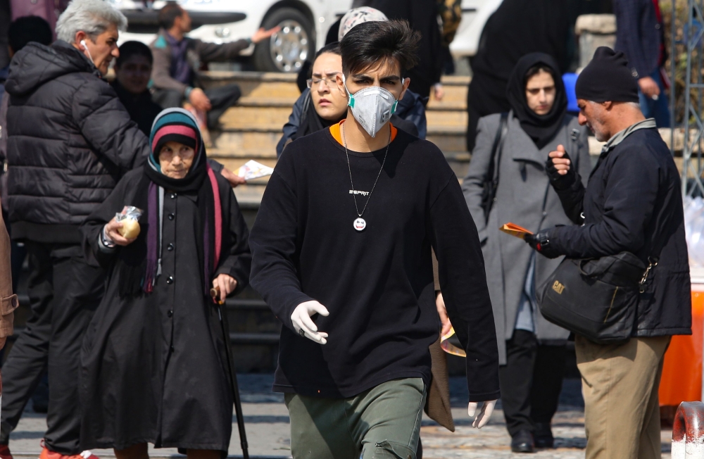 A young Iranian man wearing a protective mask, walks in a busy street in the capital Tehran on February 22, 2020.  AFP / ATTA KENARE