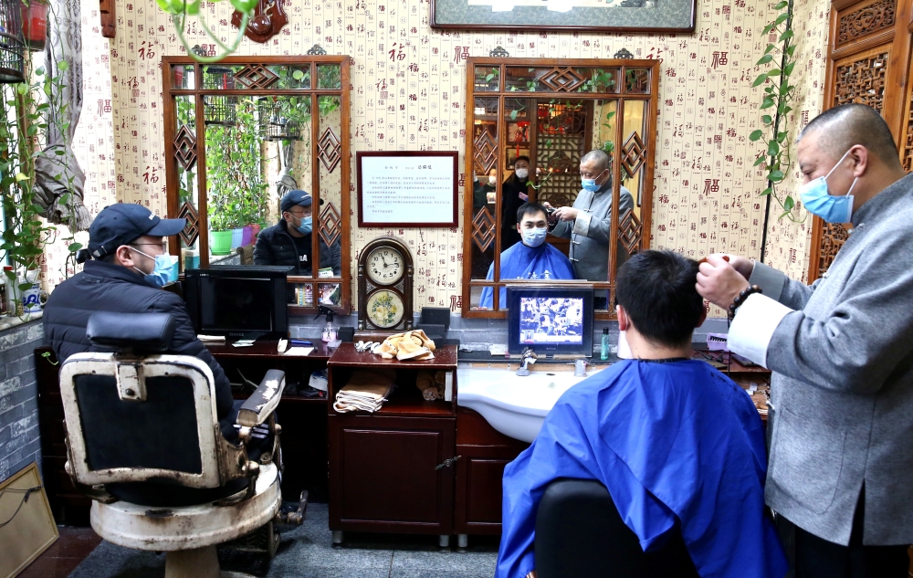 An employee wearing a face mask cuts hair for a customer at a traditional barber shop in Beijing, China February 24, 2020. China Daily via Reuters