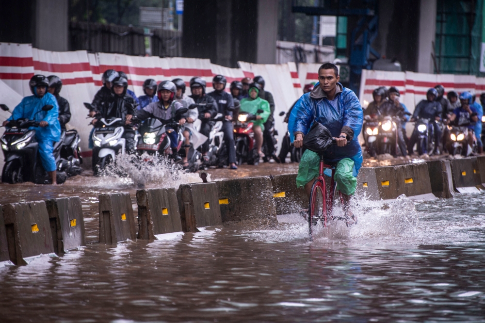 A cyclist rides alongside motorcyclists along a flooded street in Jakarta, Indonesia, February 25, 2020 in this photo taken by Antara Foto. Antara Foto/Aprillio Akbar/ via REUTERS