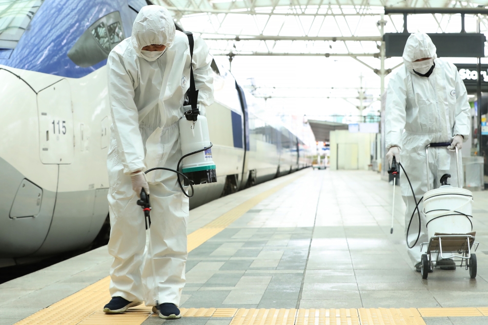 Railway workers wearing protective gear spray disinfectant as part of preventive measures against the spread of the COVID-19 coronavirus, at a railway station in Seoul on February 25, 2020. AFP / YONHAP 