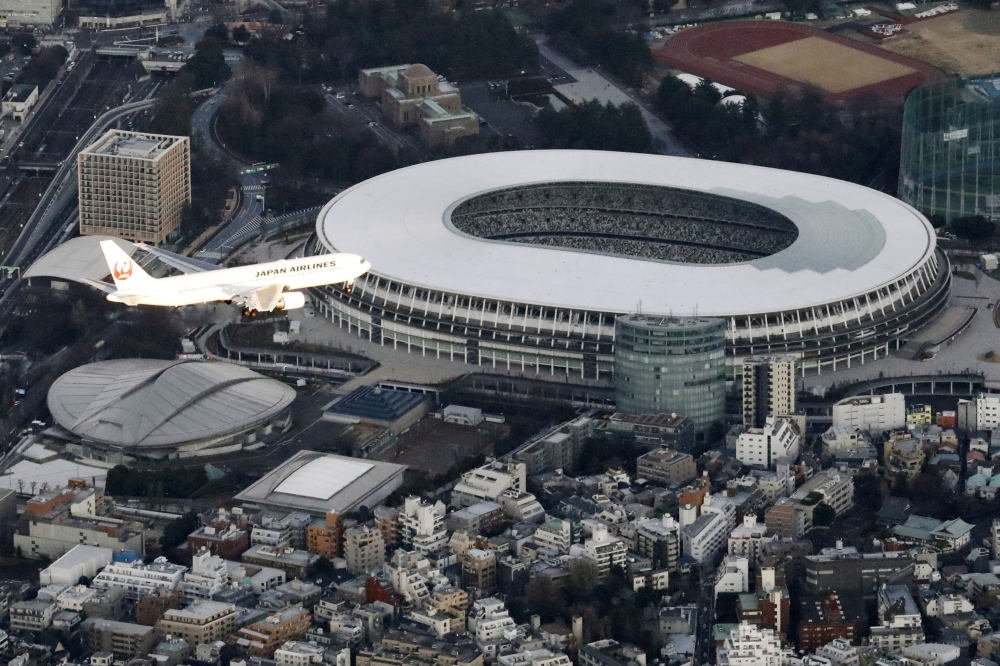 An aerial view shows an airplane flying near National Stadium in a test of the new flight paths for international passenger aircraft bound for Haneda Airport, in Tokyo, Japan February 2, 2020. Credit:  Kyodo/via Reuters  