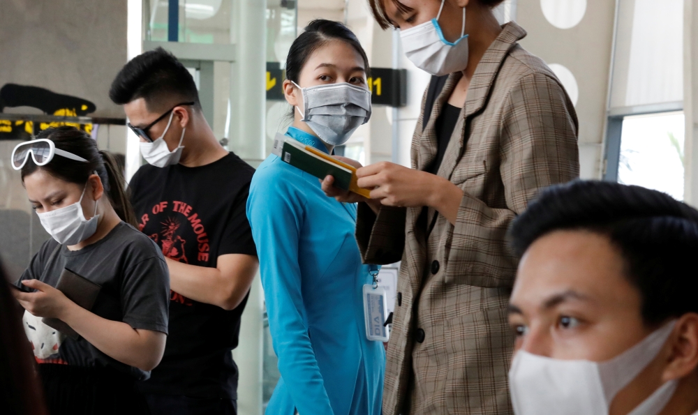  A ground staff member of Vietnam Airlines and passengers wearing protective mask, following an outbreak of the novel coronavirus, wait for boarding at the Danang airport in Danang city, Vietnam February 23, 2020. REUTERS/Kham 