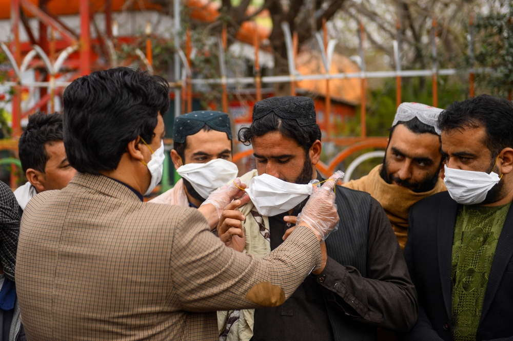 A volunteers (L) hands out free facemasks to people as a preventive measure against the spread of the COVID-19 coronavirus, in Herat city on February 26, 2020.  AFP / HOSHANG HASHIMI