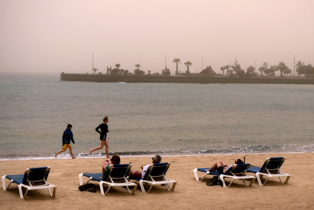 Children run along the beach as people look over the sea into the haze created by a sand storm known locally as La Calima in Arrecife, Lanzarote, Canary Islands Spain, February 23, 2020. Reuters / Russell Boyce