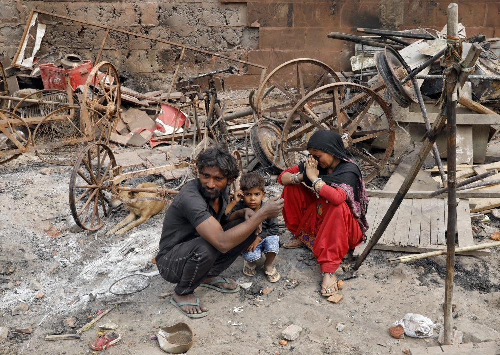 A woman sitting with her husband and their child reacts next to damaged property after their house was burnt by a mob on Tuesday in a riot affected area after clashes erupted between people demonstrating for and against a new citizenship law in New Delhi,