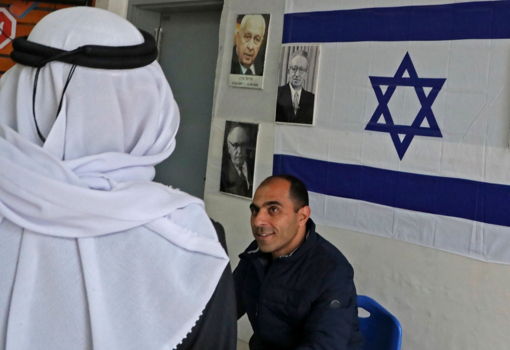 An Arab-Israeli man arrives at a poling station, decorated with portraits of Israeli politicians, to cast his ballot for the parliamentary election in the Bedouin town of Rahat near the southern Israeli city of Beersheba on March 2, 2020.  AFP / Hazem Bad