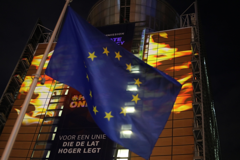 The European Union flag flies in front of images projected by activists from the environmental group Greenpeace showing Earth on fire onto the European Commission headquarters during a protest action on the eve of the presentation of the European Union cl