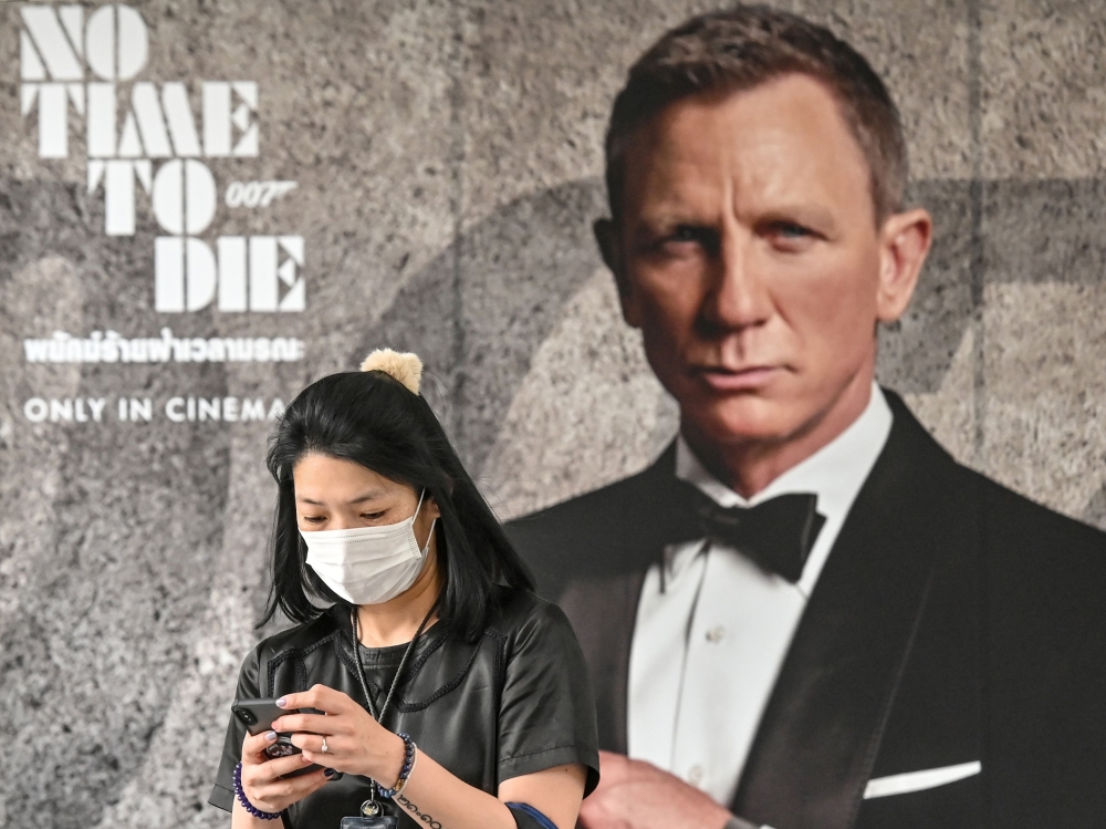 A woman wearing a facemask amid fears of the spread of the COVID-19 novel coronavirus walks past a poster for the new James Bond movie ‘No Time to Die’ in Bangkok on February 28, 2020. AFP / Mladen Antonov
 