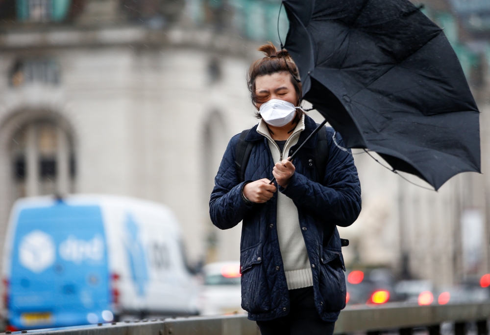 A man wearing a protective face mask walks with an umbrella in London, Britain, March 5, 2020. Reuters/Henry Nicholls