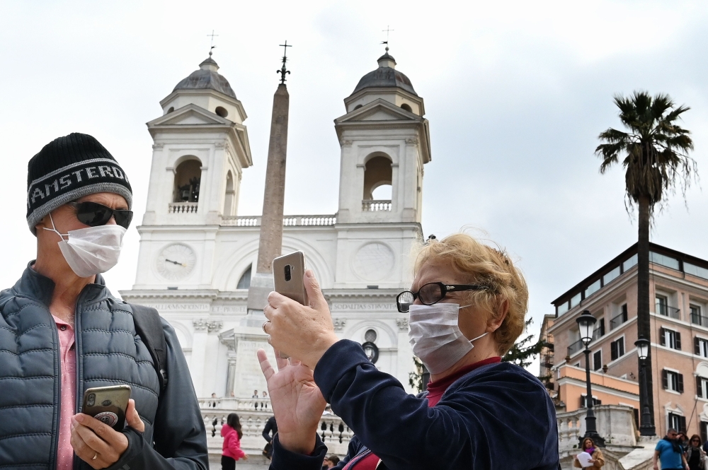 Tourists wearing protective masks looks on at Spanish Steps (Piazza di Spagna) in Rome on March 7, 2020 amid fear of Covid-19 epidemic. AFP / Alberto PIZZOLI