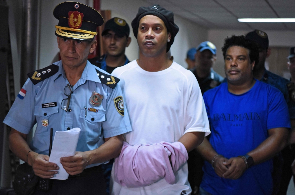 Brazilian retired football player Ronaldinho (C) and his brother Roberto Assis (R) arrive at Asuncion's Justice Palace to appear before a public prosecutor who will decide whether to grant them bail or not following their irregular entry to the country, i
