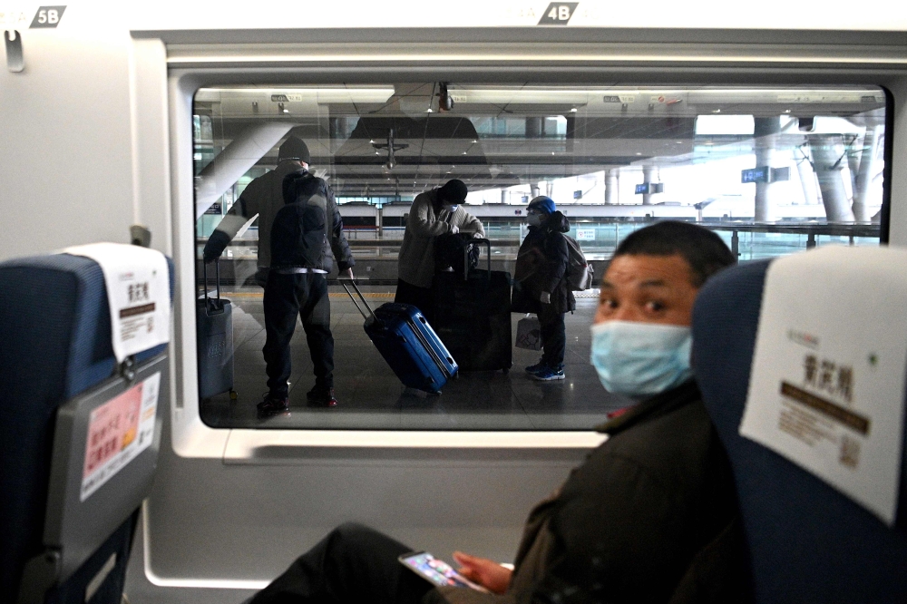 A mask-clad passenger looks on from his seat as others (background) alight from their train at the railway station in Wuhan, China's central Hubei province on March 10, 2020./ AFP / Noel Celis