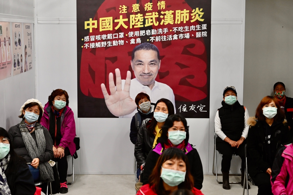 Mask-clad local residents wait in front of a poster showing New Taipei City mayor Hou You-yi during a drill organised by the New Taipei City government to prevent the spread of the COVID-19 coronavirus, in Xindian district on March 14, 2020. /AFP / Sam Ye
