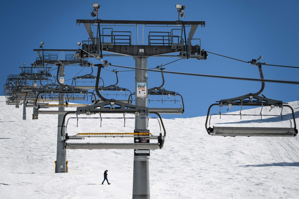  A man walks in a ski slope under a closed ski lift on Mars 15, 2020, after the Swiss government announced preventive measures against the spread of the COVID-19, (new coronavirus) in the Swiss resort of Les Crosets, next to the French border. / AFP / Fab