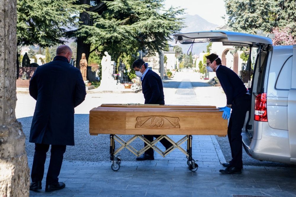 Undertakers wearing a face mask unload a coffin out of a hearse on March 16, 2020 at the Monumental cemetery of Bergamo, Lombardy, as burials of people who died of the new coronavirus are being conducted at the rythm of one every half hour. AFP / Piero Cr