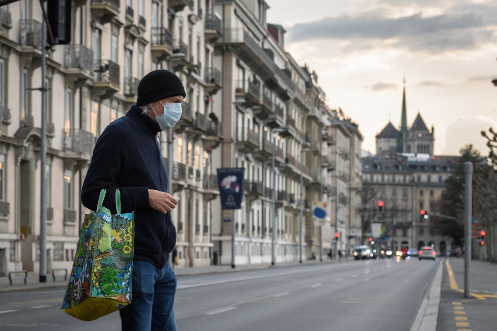 A man wearing a face mask uses a pedestrian crossing in front of Saint-Pierre Cathedral in Geneva on March 20, 2020, as the Swiss government further tightened measures against COVID-19, but said it would not follow other countries in ordering full confine