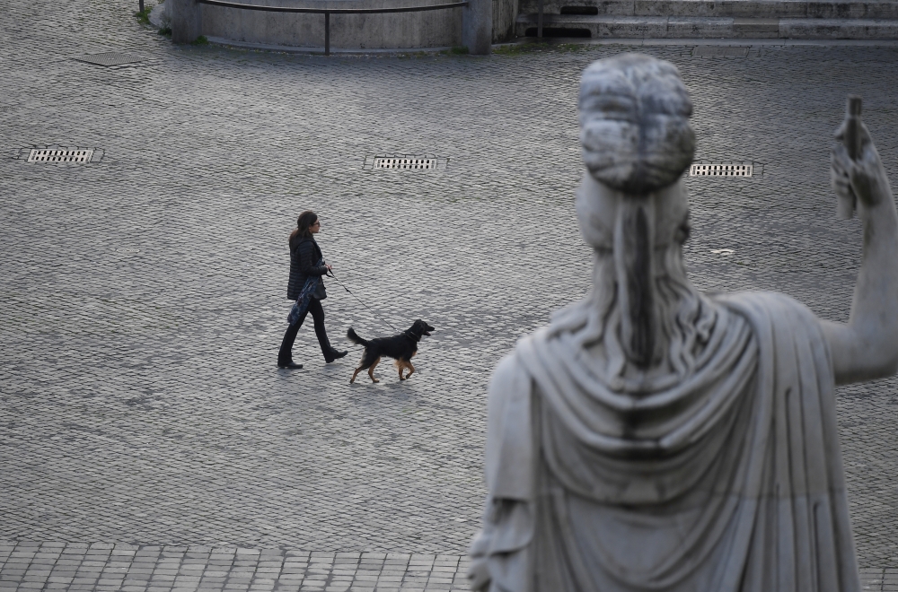 :A woman with her dog is seen crossing the deserted Piazza del Popolo while the Italians stay at home as part of a lockdown against the spread of coronavirus disease (COVID-19) in Rome, Italy March 22, 2020. REUTERS/Alberto Lingria