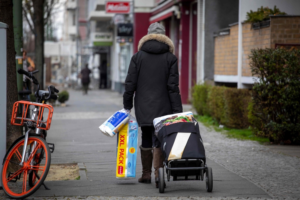 A woman carting toilet paper and kitchen rolls walks along a largely deserted Uhlandstrasse in Berlin on March 19, 2020. / AFP / Odd ANDERSEN