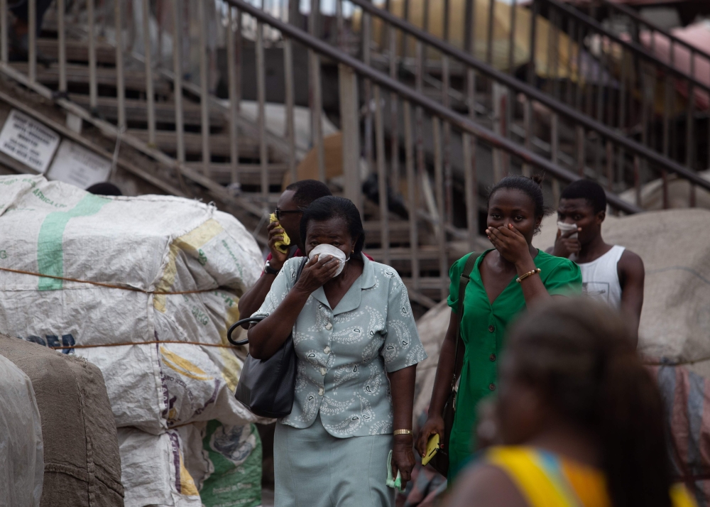 Residents protect their faces with masks and other items as a preventive measure against COVID-19 Coronavirus as city worker disinfects a market n Accra on March 23, 2020.   AFP / Nipah Dennis
