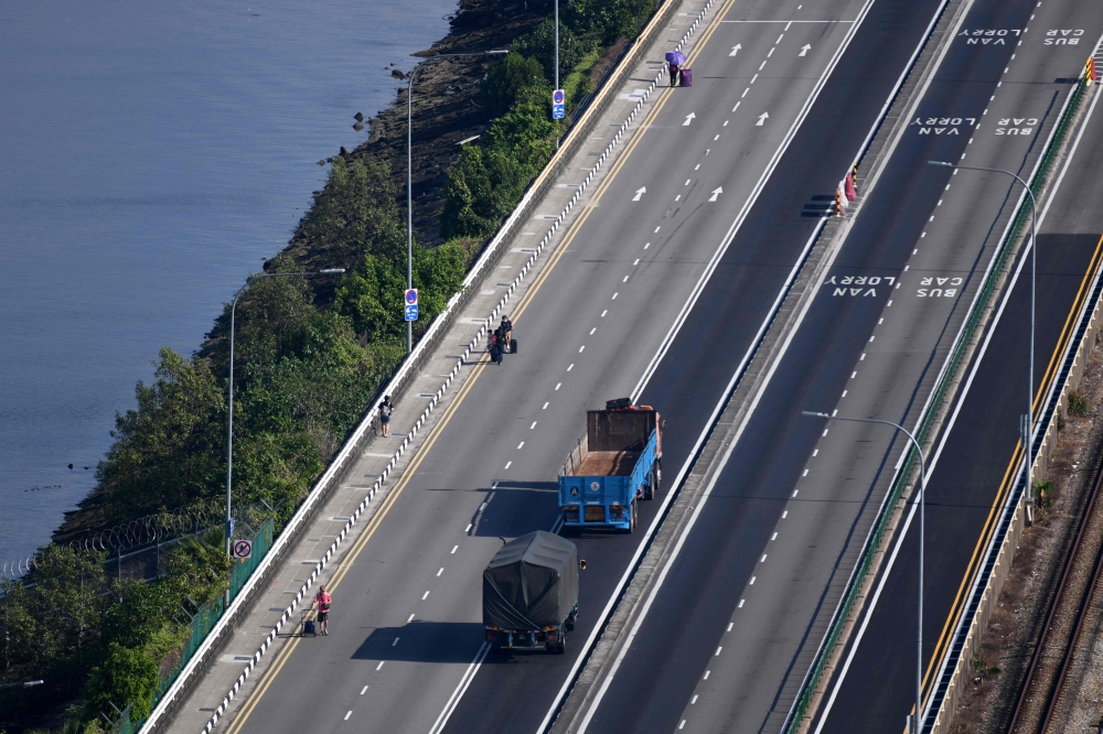 People walk across the causeway between Malaysia's southern state of Johor (top) and Singapore (bottom), as seen from Singapore, on April 1, 2020. / AFP / Roslan RAHMAN