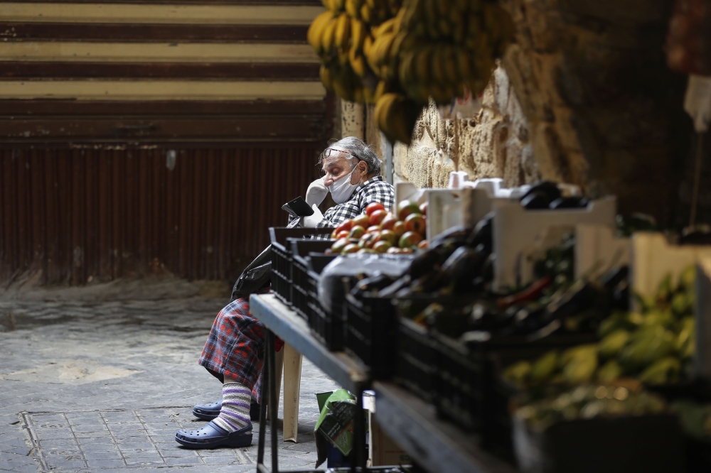 A Lebanese man sitting by a fresh produce stall checks his phone in the market of the historic part of the southern coastal city of Saida, on April 6, 2020. AFP / JOSEPH EID