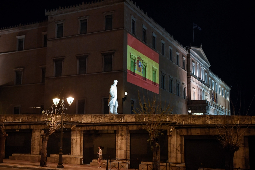 A woman jogs past the Greek parliament building in Athens, lighted with Spanish national flag colors supporting Spain in their efforts against the COVID-19 coronavirus on April 11, 2020. / AFP / Louisa GOULIAMAK