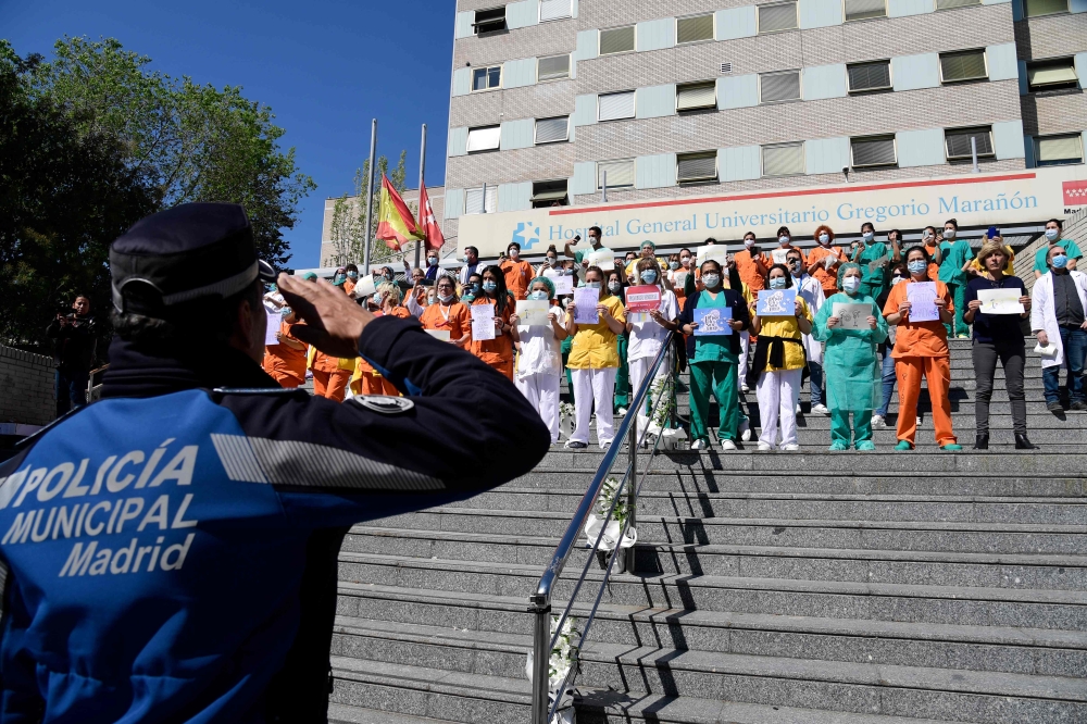 :TOPSHOT - A policeman salutes heathcare workers outside the Gregorio Maranon Hospital in Madrid on April 12, 2020, during a national lockdown to prevent the spread of the COVID-19 disease. Spain's daily death toll from the coronavirus rose to 619, after 