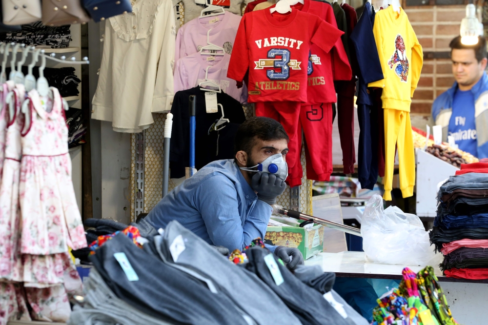 An Iranian shopkeeper wearing protective gear amid the COVID-19 pandemic watches the street from a clothes stall at the Grand Bazaar market in the capital Tehran, on April 18, 2020. AFP / ATTA KENARE
