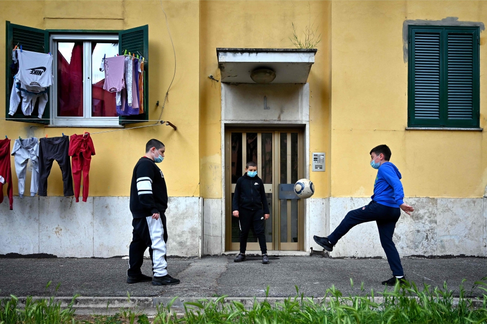 TOPSHOT - Children wearing protective face masks play football in front of their building in rome's neighbourhood of San Basilio on April 18, 2020, during the country's lockdown aimed at stopping the spread of the novel coronavirus COVID-19. / AFP / Alber
