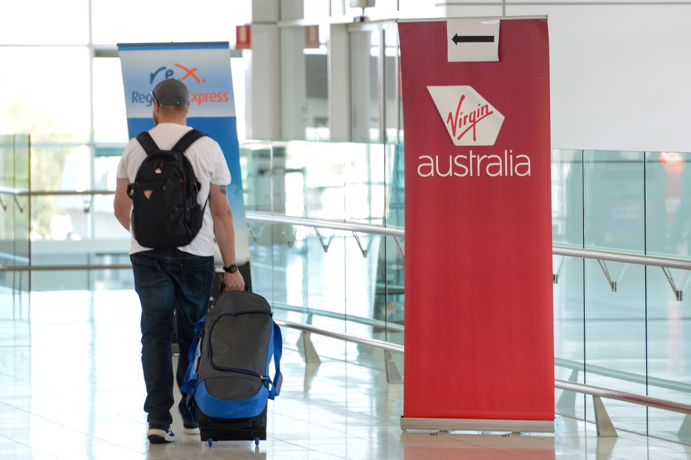 A traveller walks past a sign for Virgin Australia in the departures area at Adelaide Airport in Adelaide on April 21, 2020. AFP / Brenton Edwards 