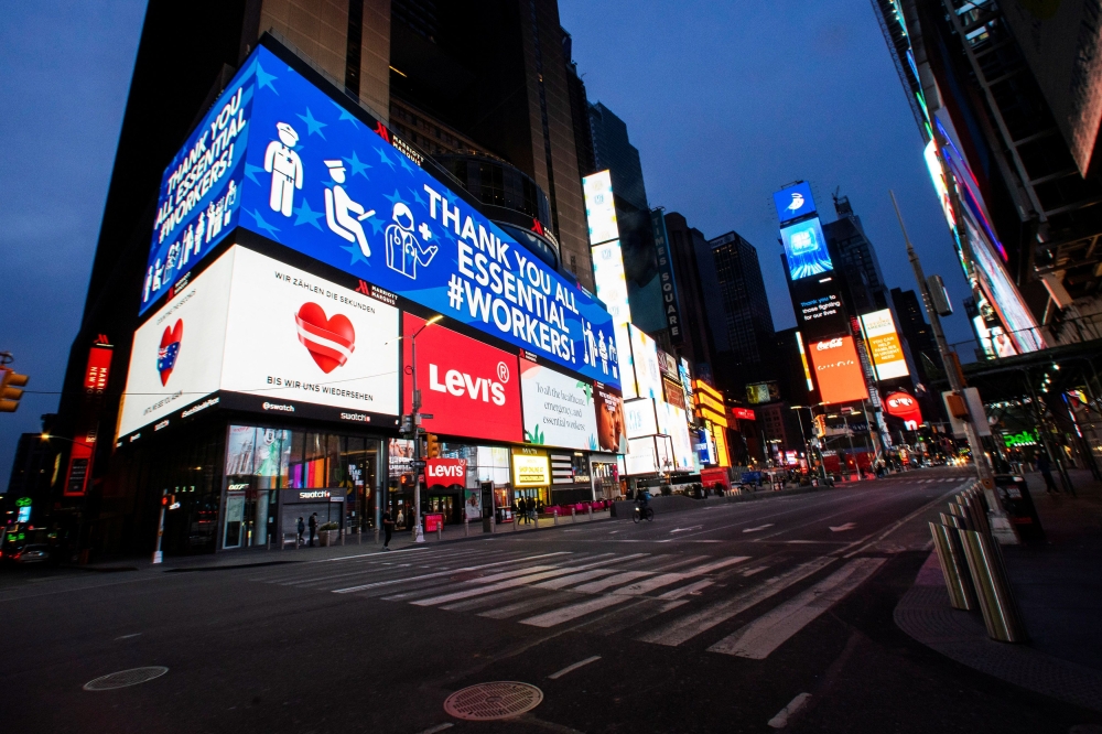 People walk round Times Square as some screens are illuminated in blue as part of the 
