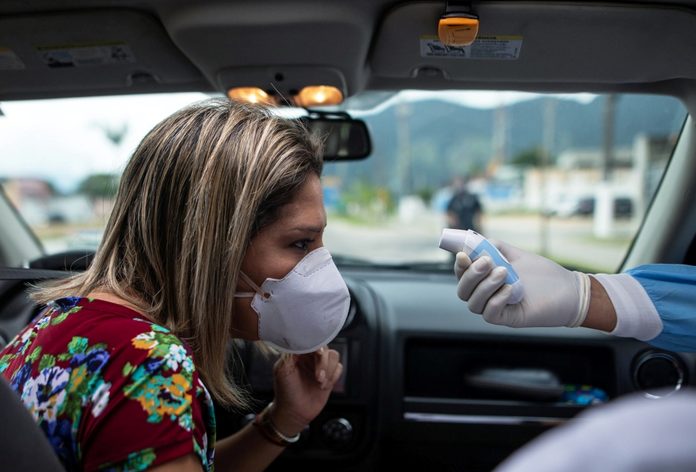 A health worker, controls the temperature of a woman in a sanitary barrier during the coronavirus disease (COVID-19) outbreak, in Sao Sebastiao, Sao Paulo state, Brazil, April 18, 2020. REUTERS/Roosevelt Cassio