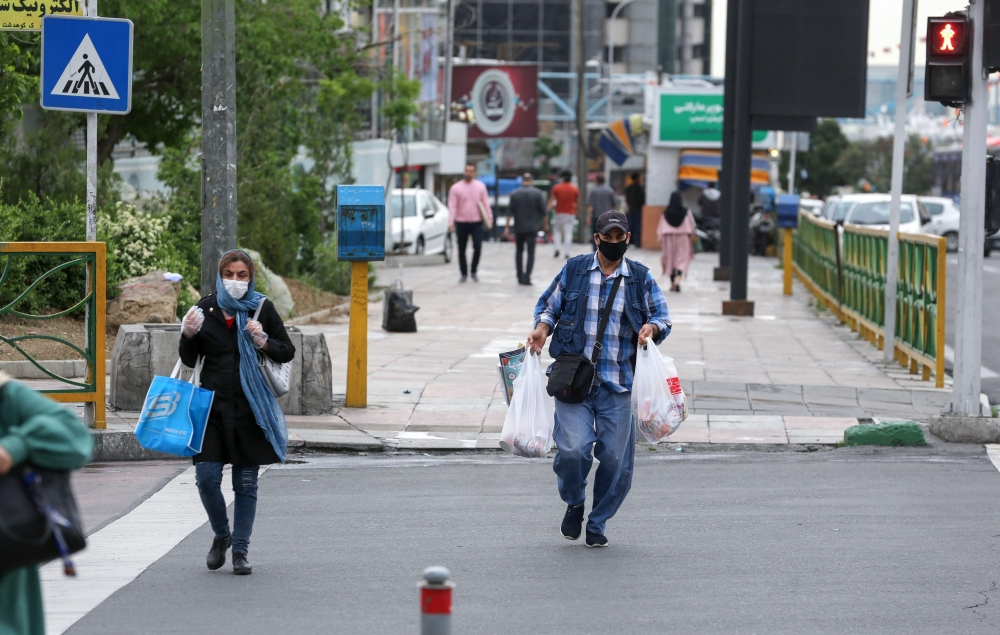 Iranians wearing protective masks amid the COVID-19 pandemic, cross a street in the capital Tehran, on April 26, 2020. / AFP / ATTA KENARE