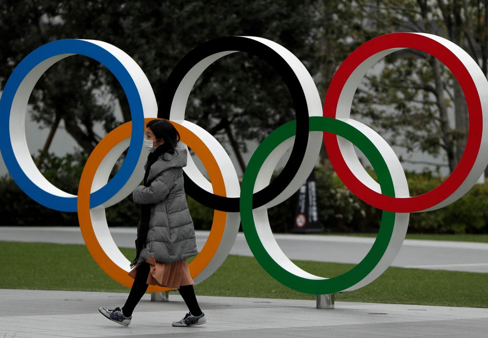 :FILE PHOTO: A woman wearing a protective face mask, following an outbreak of the coronavirus disease (COVID-19), walks past the Olympic rings in front of the Japan Olympics Museum, in Tokyo, Japan March 30, 2020. REUTERS/Issei Kato/File Photo