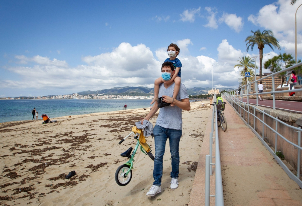 A father carries his son on his shoulders at Can Pere Antoni Beach in Palma de Mallorca, on April 26, 2020 during a national lockdown to prevent the spread of the COVID-19 disease. / AFP / JAIME REINA