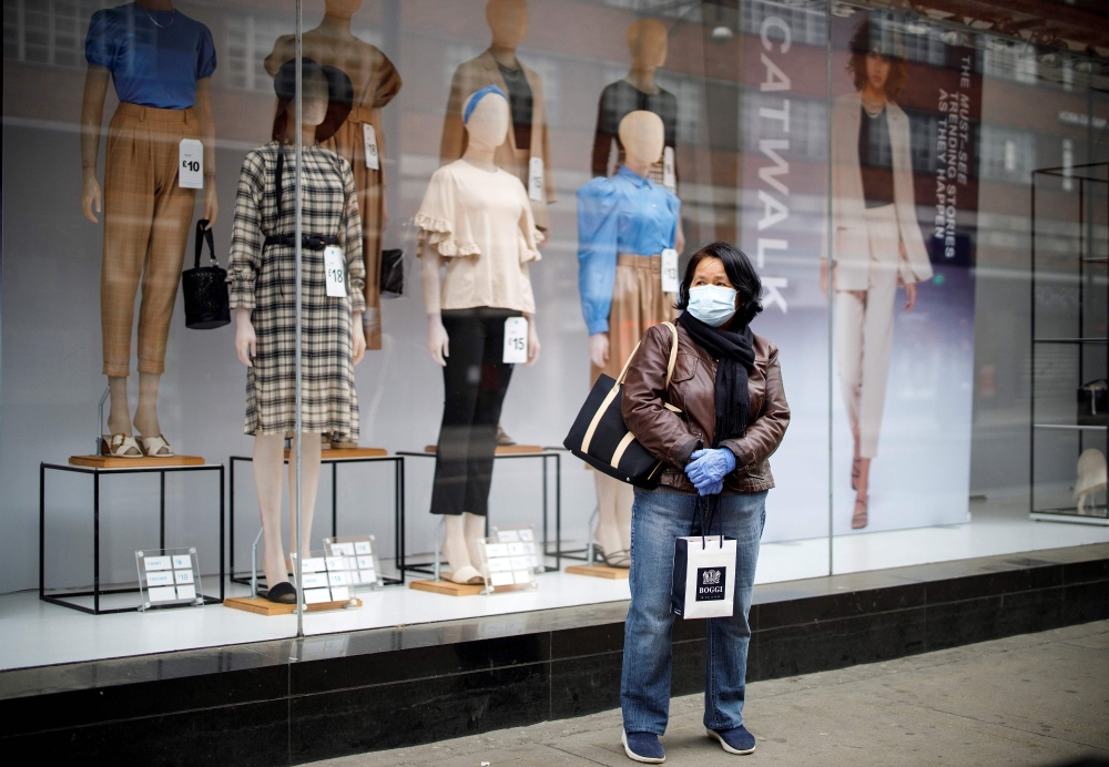 A woman wearing PPE (personal protective equipment), of a face mask as a precautionary measure against COVID-19, stands outside a Primark clothing store, closed-down due to COVID-19, on Oxford Street in central London on April 27, 2020.  AFP / Tolga AKMEN