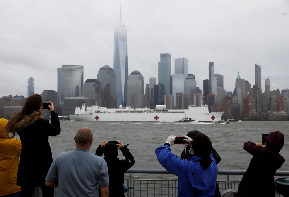 Spectators on the New Jersey shoreline take pictures as the U.S. Navy hospital ship USNS Comfort departs Manhattan and passes lower Manhattan and the World Trade Center building under heavy fog as it leaves to return to its home port of Norfolk, Virginia,