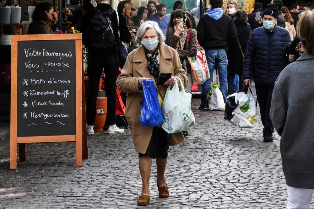 A woman wearing a protective facemask walks in the Aligre street as she does her grocery shopping during the food market, on May 2, 2020, in Paris, during the 47th day of a strict lockdown in France aimed at curbing the spread of the COVID-19 (the novel c