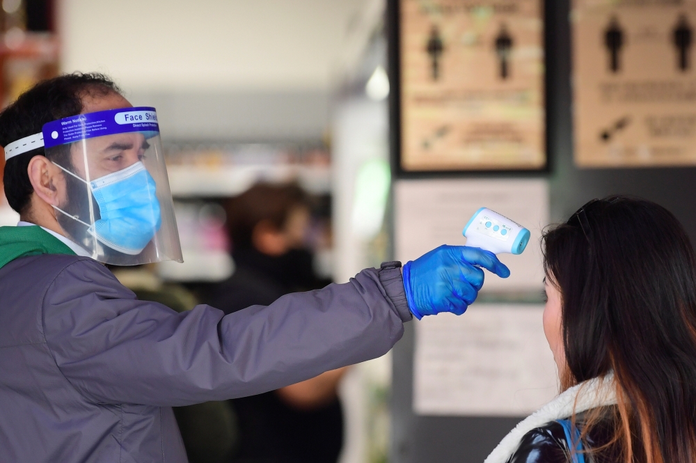 An employee takes the temperature of a customer at the entrance of a super market in China Town in London, following the outbreak of the coronavirus disease (COVID-19), London, Britain, May 2, 2020. Reuters/Toby Melville