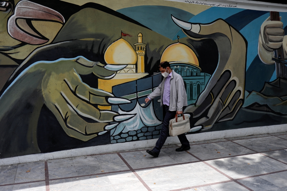 A man wearing a protective face mask walks past a Palestine mural on the wall following the outbreak of the coronavirus disease (COVID-19), in Tehran, Iran, April 30, 2020. 