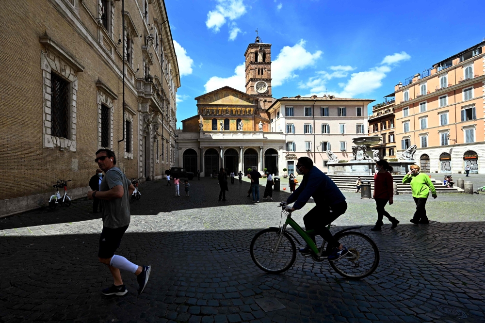 A man rides his bike as another jogs past Rome's Santa Maria in Trastevere square on May 3, 2020, during the country's lockdown aimed at curbing the spread of the COVID-19 infection, caused by the novel coronavirus.  AFP / Vincenzo PINTO
