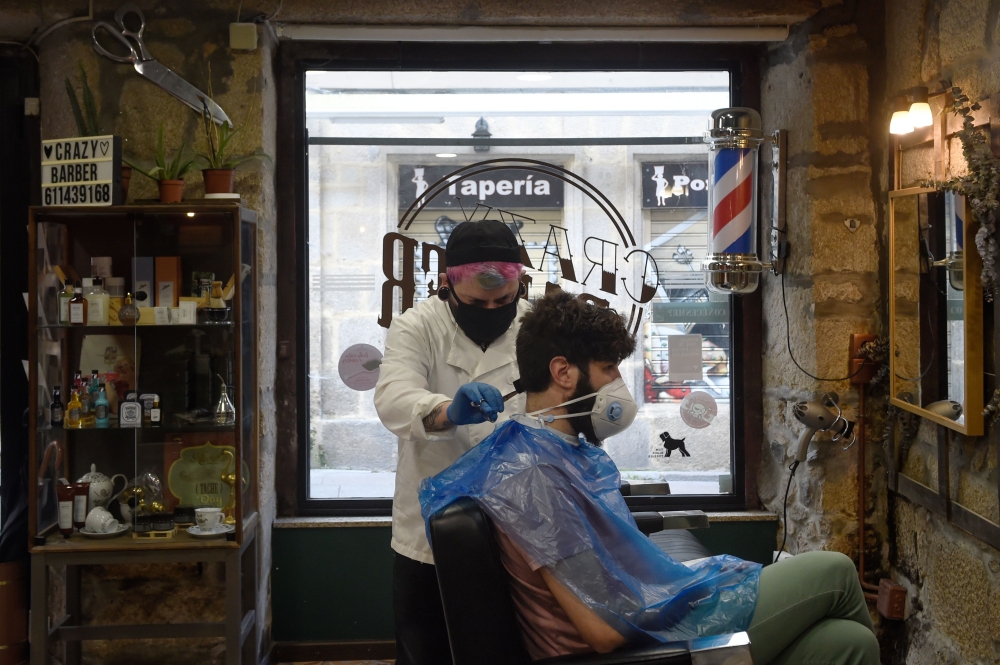:Hairdresser David Cores cuts his first client's hair after reopening his barber shop in Pontevedra, on May 4, 2020, for the first time since the beginning of a national lockdown to prevent the spread of the COVID-19 disease./ AFP / MIGUEL RIOPA
