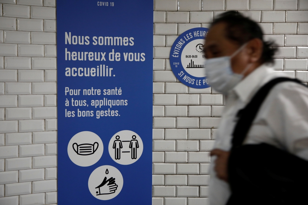 A wearing a protective face mask walks past a placard with health and social distancing informations at a metro station of Paris transport network (RATP) during the outbreak of the coronavirus disease (COVID-19) in Paris, France, May 5, 2020. REUTERS/Beno