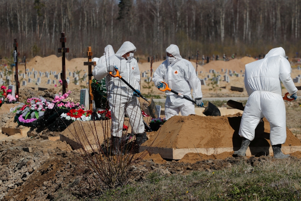 Grave diggers wearing personal protective equipment (PPE) bury a coronavirus disease (COVID-19) victim in the special purpose section of a graveyard on the outskirts of Saint Petersburg, Russia May 5, 2020. REUTERS/Anton Vaganov