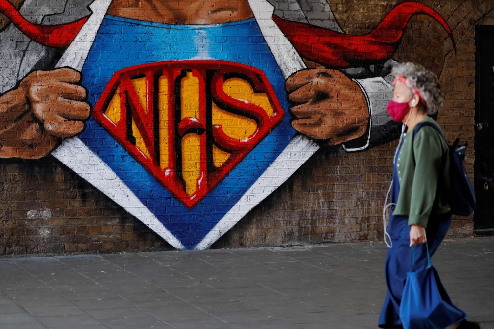A woman wearing a facemask passes an artwork celebrating the National Health Service (NHS) painted on a brick wall in central London on May 5, 2020, during the nationwide lockdown due to the novel coronavirus COVID-19 outbreak. / AFP / Tolga AKMEN
